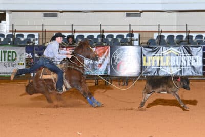 Cowboy roping a steer during a rodeo event at an indoor arena with spectators in the background