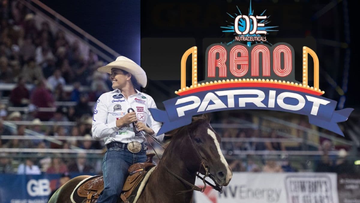 Rodeo competitor on horseback wearing white hat and western attire rides past "Brand Patriot" signage at indoor arena event