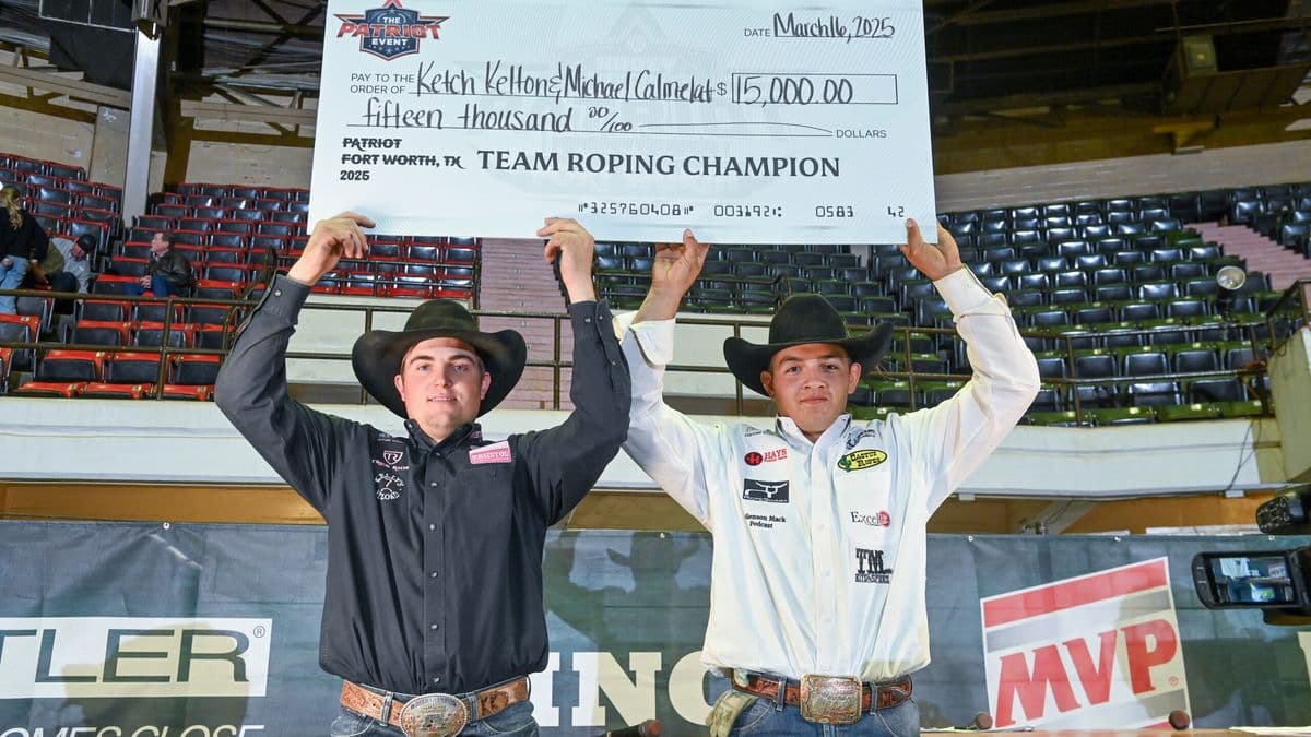 Two team roping champions hold a large ceremonial check for $15,000 at the 2025 Patriot Fort Worth event in an indoor arena