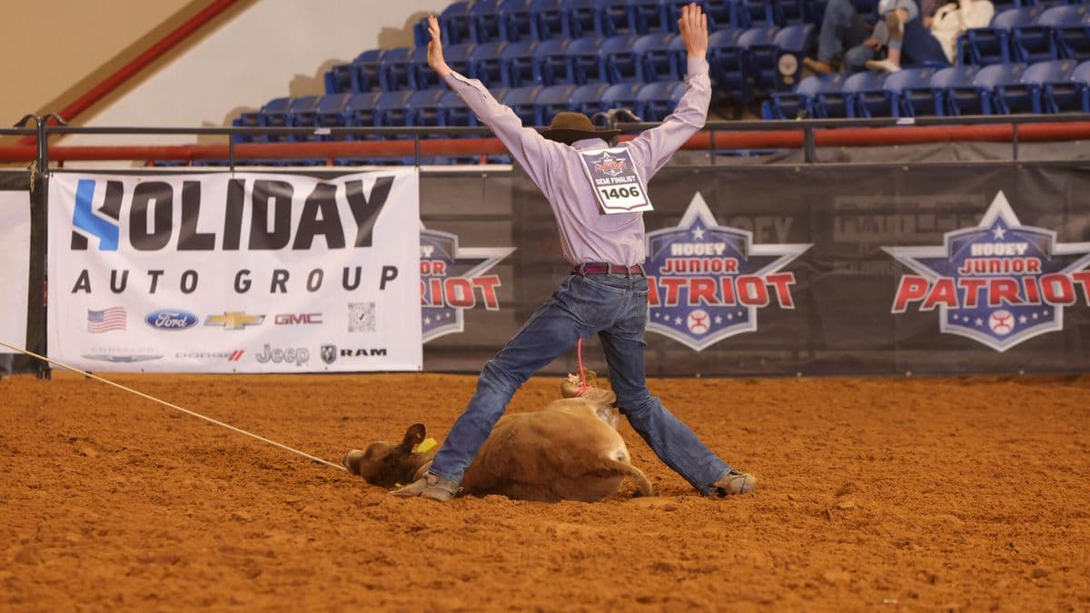 Steer roper celebrates with arms raised after successfully roping a steer at a junior rodeo event in an indoor arena