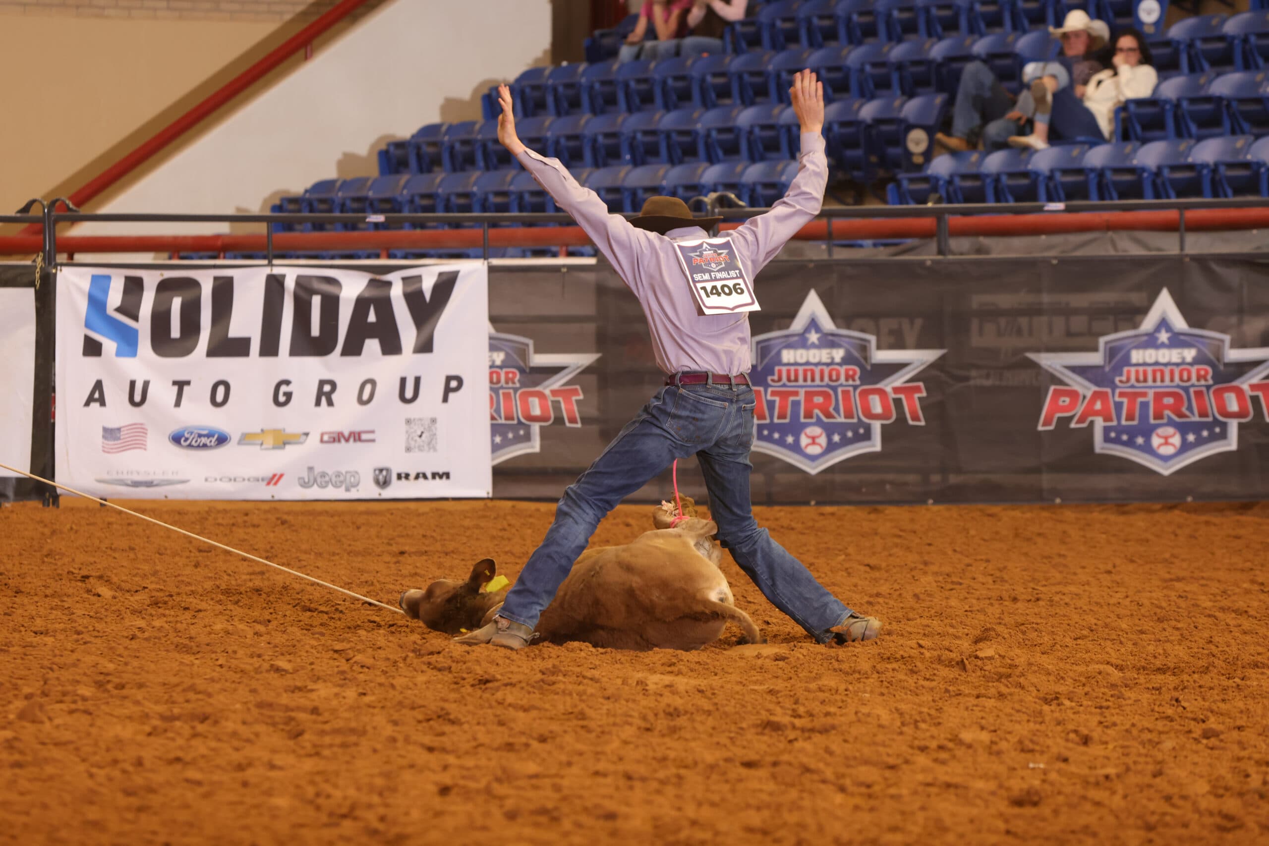 Steer roper celebrates with arms raised after successfully roping a steer at a junior rodeo event in an indoor arena